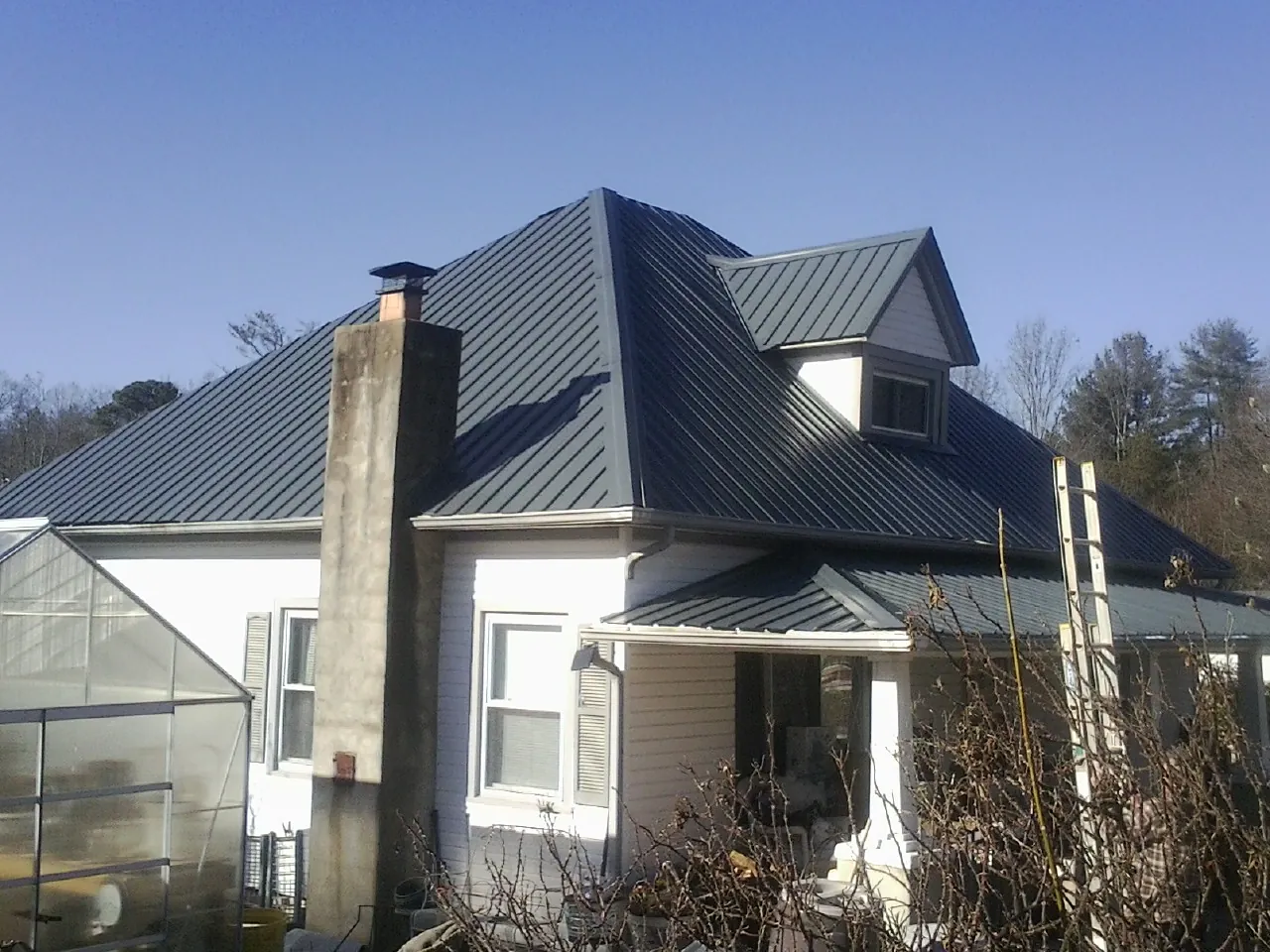 Dark blue standing seam metal roof on a white farmhouse with dormer — Slate & Tile Roof Repair by Roofing Brothers in Mills River