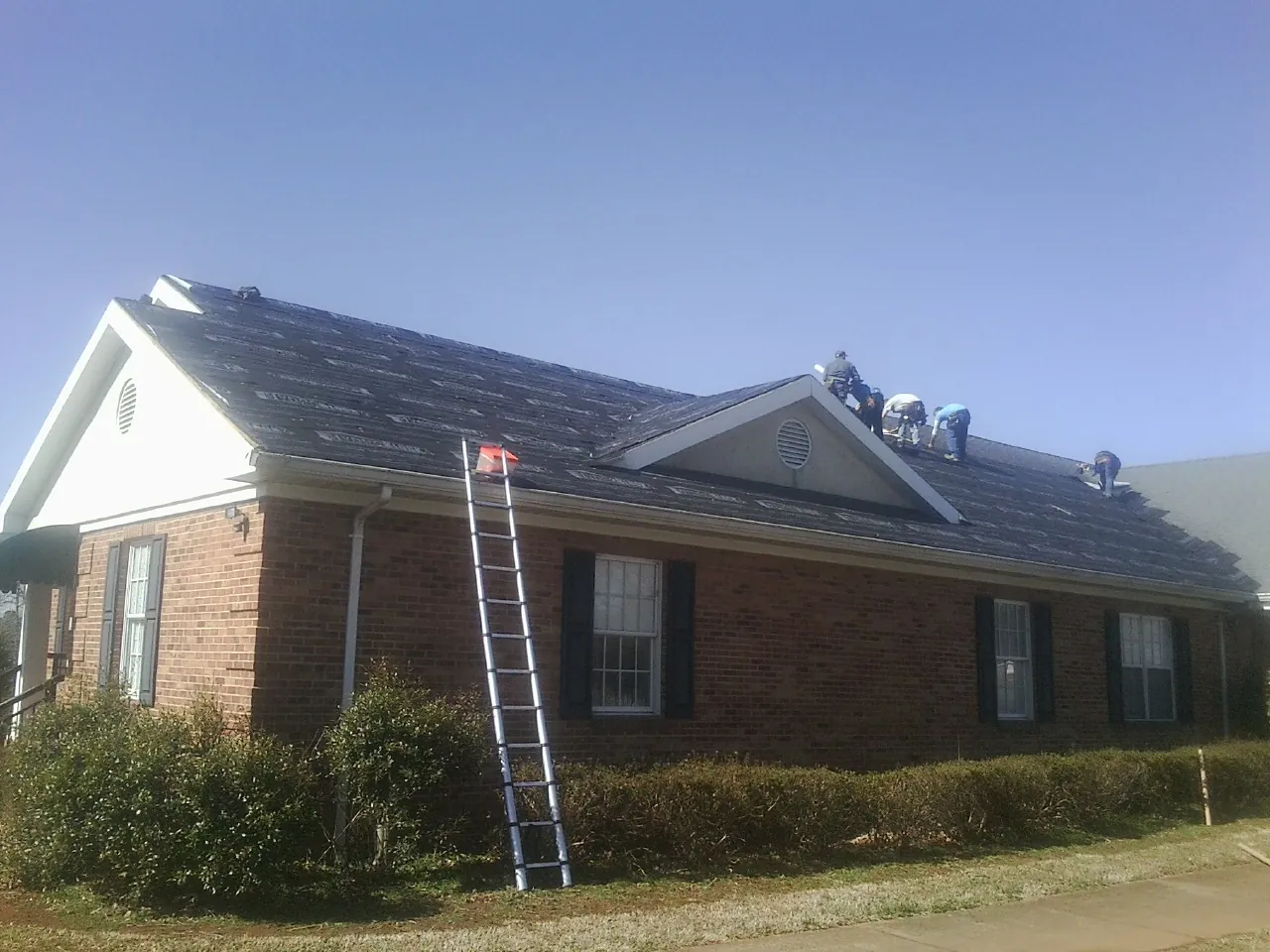 Crew tearing shingles off a brick ranch roof with a ladder set — Emergency Roof Repair work by our crew in Mills River