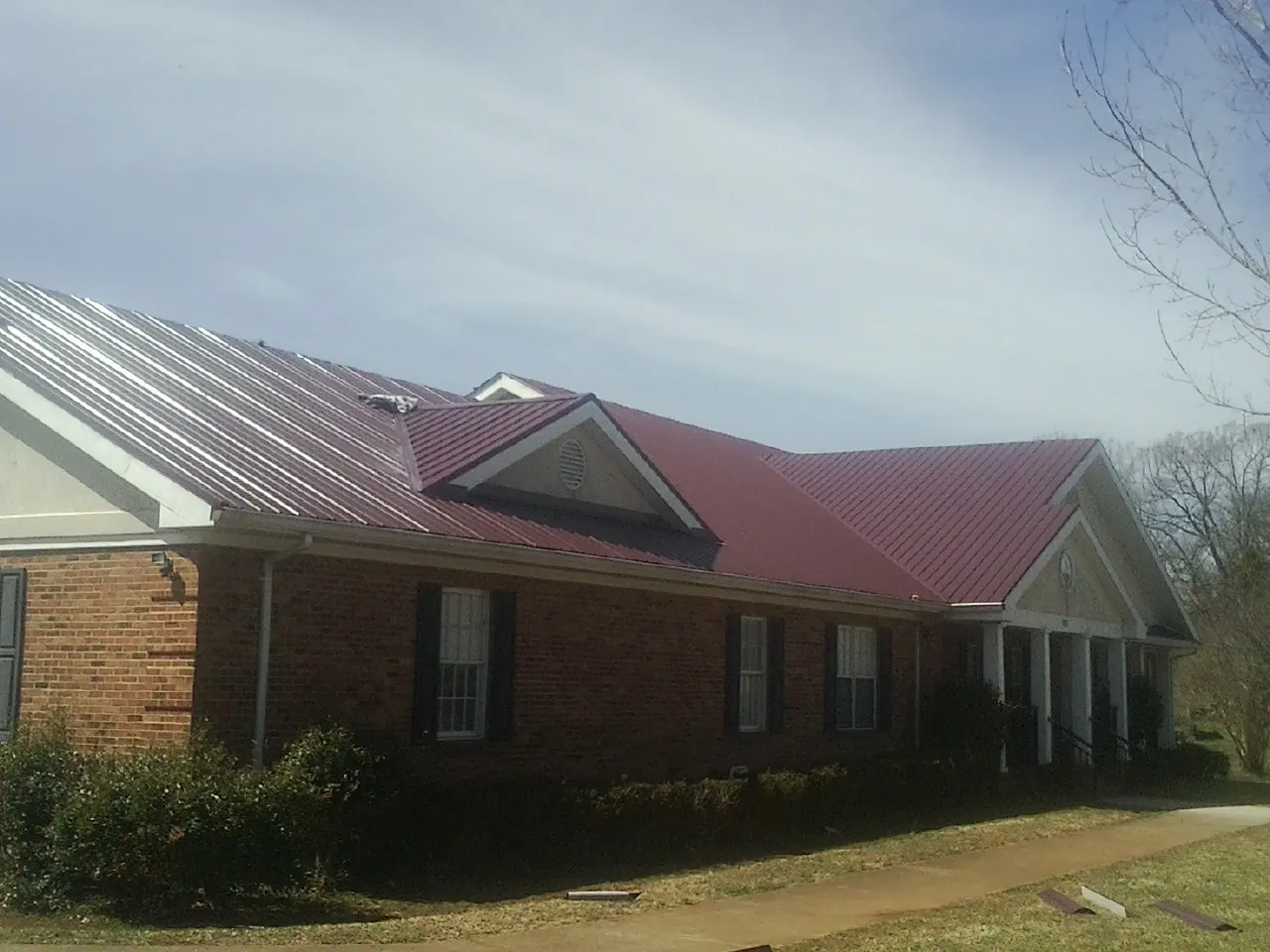 Red metal roof with gabled entries on a long brick building, from a Hail Damage Roof Repair job in Mills River