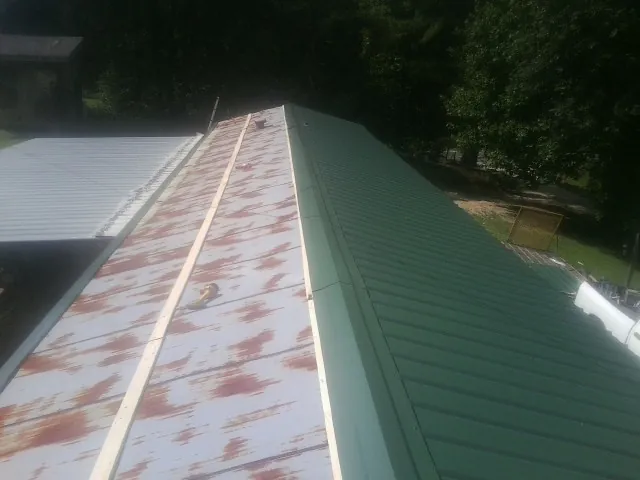 Old rusted panels beside newly installed green metal roofing — Wind Damage Roof Repair by Roofing Brothers in Mills River