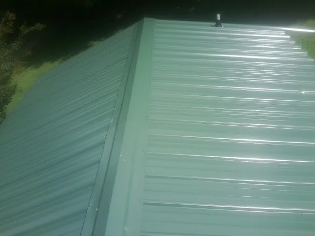 New green metal panels meeting at the ridge of a roof — Flat Roof Repair work by our crew in Mills River