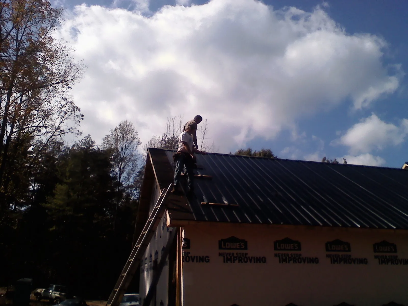 Roofer fastening dark metal panels high against a cloudy sky, from a Roof Inspection job in Mills River