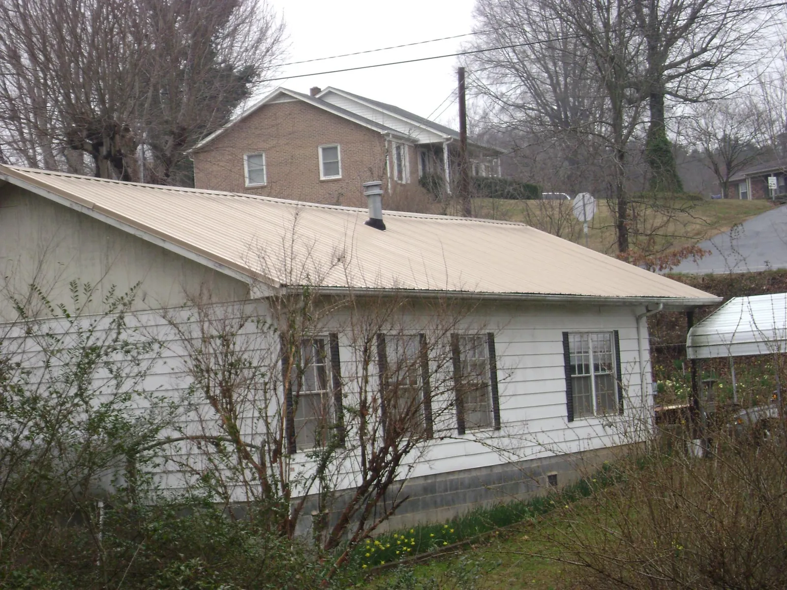 Tan metal roof on a white sided house set into a hillside — Commercial Roofing by Roofing Brothers in Mills River