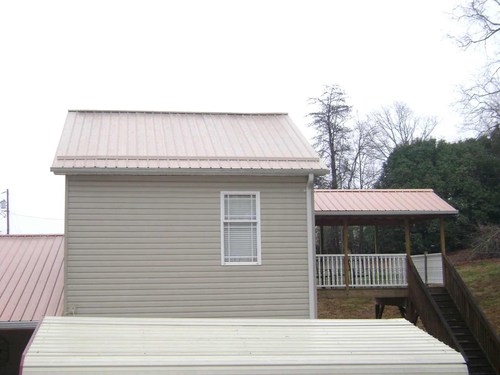 Tan metal roofs on a two story addition and attached porch, from a Roof Replacement job in Mills River